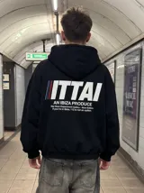 Hoodie negro de corte holgado con capucha y bolsillo frontal tipo canguro. Presenta un estampado gráfico en la espalda con el texto 'ITTAI AN IBIZA PRODUCE' y detalles en colores azul, blanco y rojo.