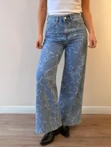 Jeans de corte wide leg y tiro alto, confeccionados en denim celeste con estampado de lazos en tono claro. Presentan cierre frontal con botón y cierre metálico, además de bolsillos funcionales.