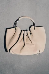 Bolso tipo saca de serraje color beige con doble asa rígida asimétrica y asa bandolera extraíble. Incluye cartera con bolsillo extraíble.