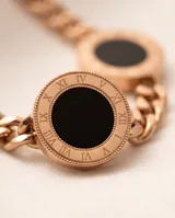 Collar de cadena de eslabones en acero con baño de oro rosa, que presenta tres dijes circulares con centro de ónix negro y bordes grabados con números romanos.