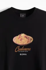 Remera negra de punto de algodón de peso medio, corte holgado con hombros caídos, cuello redondo ribeteado y bajo recto. Presenta un estampado frontal centrado de un plato de pasta carbonara con las inscripciones "Carbonara Uova Guanciale Pecorino" y "ROMA".