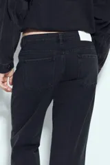 Pantalón de jean negro de tiro medio y corte recto, con diseño de cinco bolsillos y cierre frontal con botón y cremallera.