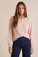 Blusa de corte oversize con estampado de rayas verticales finas, cuello redondo con pequeña abertura y cierre frontal de botones. Presenta mangas largas con puños ajustados y detalle de frunces en la parte superior.