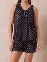 Conjunto de pijama de dos piezas, compuesto por una musculosa sin mangas con escote en V y botones frontales, y un short. Ambas prendas son de tejido soft estampado en color negro con diseño de pequeños círculos claros.