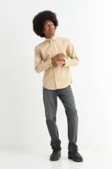 Camisa de manga larga en color beige, confeccionada en algodón, con cuello clásico y cierre frontal de botones.