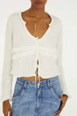 Blusa blanca de manga larga con escote en V, detalles de volados horizontales y cierre frontal con tiras ajustables.