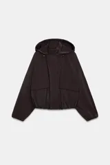 Cazadora de cuello subido con capucha ajustable, manga larga con puños elásticos y bajo elástico. Cuenta con bolsillos delanteros y cierre frontal con cremallera oculta y botones a presión.
