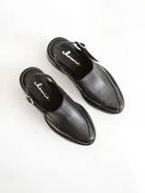Zapato tipo slingback color negro, con plataforma y taco cuadrado. Presenta una puntera cuadrada y cierre con hebilla metálica en la tira trasera.