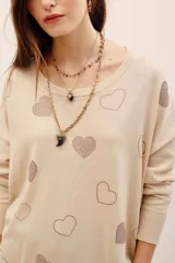 Sweater tejido de punto color beige con diseño holgado, cuello redondo, manga larga y aplicación de corazones formados con tachas brillantes en contraste.