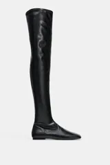 Bota mosquetera de caña extra larga, color negro, con diseño ajustado y suela plana. Presenta punta redonda y cierre lateral.