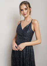 Vestido largo de fiesta con escote en V cruzado y breteles finos. Confeccionado en tela negra con acabado de glitter brillante, presenta un corte entallado en la cintura y falda con caída fluida.