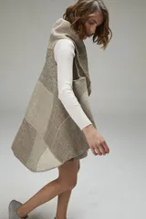 Chaleco sin mangas de tejido de lana fina sin teñir, con diseño circular y bloques de color beige y marrón. Presenta un cuello amplio y solapa que permite usarlo como chaleco largo o capa corta.