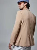 Saco color beige de piqué con cuello con solapas y bolsillos de plastrón. Mangas con coderas y bajo con abertura en espalda.