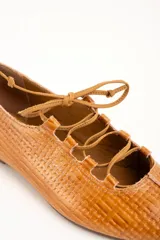 Zapatos planos de cuero color caramelo, con textura trenzada, cordones frontales en el empeine y punta redondeada.