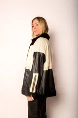 Campera con cuerpo de corderito color beige, mangas y parte inferior de cuero sintético negro con textura tipo cocodrilo. Tiene cuello estilo camisa con solapas de corderito negro, cierre frontal con cremallera y bolsillos laterales.