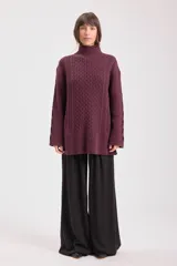 Sweater de punto color bordó con cuello alto y diseño de trenzas en el frente y las mangas. Presenta un corte holgado y largo, con puños y ruedo acanalados.