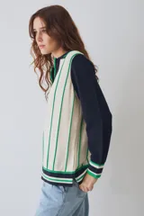 Remera tejida de punto estilo polo con mangas largas en color crema y cuerpo en color bordó con rayas verticales amarillas. Presenta cuello tipo polo, aberturas laterales y un pequeño parche circular con diseño de sol en el pecho.