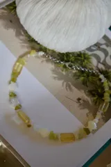 Gargantilla corta con cuentas de piedra irregulares en tonos amarillo pálido y beige, combinadas con cuentas facetadas rectangulares. Incluye un segundo collar con eslabones grandes dorados y un dije con forma de herradura dorada.