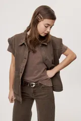 Pantalón jean de tiro medio, color negro, de corte amplio y silueta extra wide leg. Presenta diseño clásico de cinco bolsillos, cierre frontal con botón y cremallera, y detalle de tachas metálicas aplicadas a lo largo de los laterales.