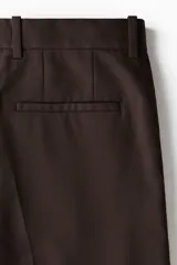Pantalón sastrero de sarga en color marrón oscuro, con corte holgado, piernas amplias con raya marcada, cierre frontal con botón y corchete ocultos, bolsillos laterales al bies y bolsillos traseros insertados.