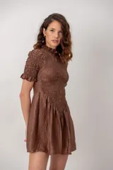 Vestido corto color marrón chocolate, con cuerpo fruncido tipo nido de abejas, cuello alto con volados y mangas cortas abuchonadas con terminación en volado. Presenta falda evasé con vuelo.