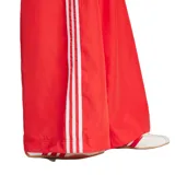 Pantalon Adidas de corte ancho y tiro alto, color rojo, con cintura elástica ajustable mediante cordón. Presenta las icónicas tres tiras blancas laterales y el logo del trébol bordado en la parte superior.