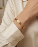 Pulsera tipo esclava rígida de acero con baño de oro, compuesta por tres bandas paralelas y un detalle central cuadrado adornado con circonias.