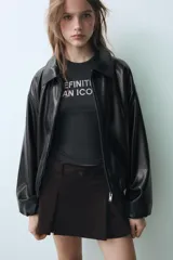 Cazadora de efecto piel en color negro, con cuello solapa, cierre frontal de cremallera metálica, bolsillos laterales de vivo y mangas largas con puños elásticos.