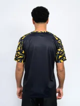 Remera deportiva de hombre, color negro, con cuello redondo y mangas cortas con estampado geométrico en amarillo y gris. Lleva el escudo de Peñarol en el pecho.