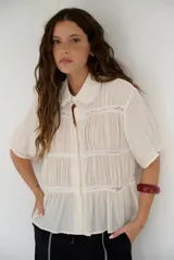 Camisa beige de manga corta con cuello camisero, cierre frontal con botones y detalles de encaje y frunces horizontales.