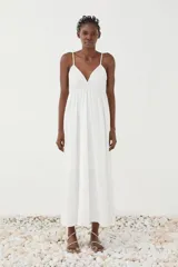 Vestido largo blanco de tirantes finos con escote en V, cuerpo fruncido bajo el busto y falda amplia de caída suave.