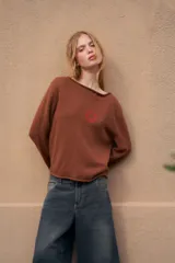 Sweater de tejido de punto color marrón, crop, con mangas largas y cuello redondo. Presenta un pequeño bordado rojo en el pecho y en el borde inferior.