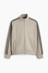 Campera deportiva de color gris topo, con cuello alto, cierre frontal bidireccional y bolsillos laterales. Presenta franjas laterales negras en las mangas y puños y bajo de punto acanalado.