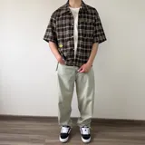 Camisa de manga corta de corte boxy fit, con estampa a cuadros en tonos marrones, azules y blancos. Cuenta con cierre frontal de botones y un bolsillo ojal en el pecho.