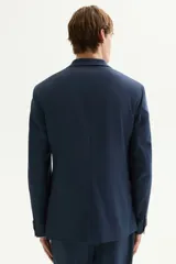Blazer azul marino de corte slim fit, con solapas de muesca finas, botonadura sencilla de un botón visible, bolsillo superior insertado y dos bolsillos delanteros con solapa. Presenta abertura doble en la espalda y forro interior.