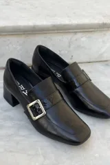 Mocasín de cuero vacuno color bordó con acabado charolado, punta cuadrada, taco bloque bajo y detalle de tira con hebilla metálica plateada en el empeine.