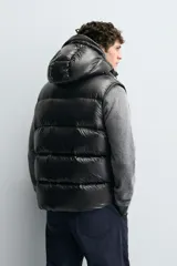 Chaleco acolchado de tejido técnico con acabado brillante y relleno de pluma y plumón. Presenta cuello subido con capucha ajustable, cierre frontal con cremallera y bolsillos laterales de vivo. Diseño resistente al viento, repelente al agua y transpirable.