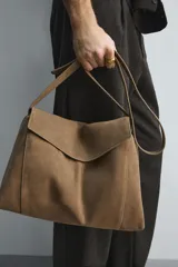 Bandolera de piel con acabado en serraje, diseño rectangular con solapa frontal y cierre magnético. Cuenta con un asa larga ajustable y compartimento interior con cierre de cremallera.