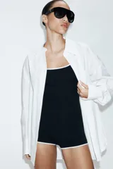 Camisa oversize de cuello solapa, manga larga con hombro caído y puños con pliegues. Presenta un bolsillo de plastrón en el frente, detalle de pinza con trabilla y botón en la espalda, bajo asimétrico y cierre frontal con botones.