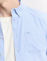 Camisa de corte clásico confeccionada en tejido oxford, con diseño de rayas verticales en tonos azul y blanco. Presenta cuello abotonado, cierre frontal con botones y bolsillo en el pecho con detalle de etiqueta bordada.