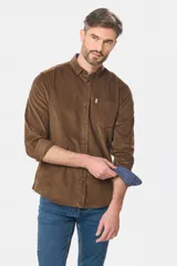Camisa de pana fina en color verde oscuro, de manga larga con puños arremangados, cuello camisero con botones y un bolsillo aplicado en el pecho con pequeña etiqueta decorativa.