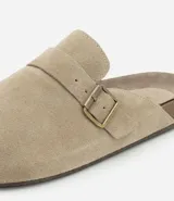Ojota mule color beige confeccionada en cuero, con tira ancha y hebilla metálica.