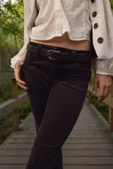 Pantalón acampanado de pana suave de algodón, color marrón oscuro. Presenta un corte ajustado de cintura a cadera y acampanado desde la rodilla al bajo. Es un modelo de tiro bajo con cierre y botón, con bolsillos abiertos delanteros y bolsillos traseros con solapa y botón.