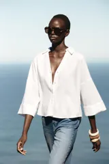 Camisa blanca de lino con cuello solapa, escote pico, manga ancha por debajo del codo con vuelta y bajo asimétrico.