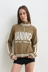 Campera de punto de algodón color marrón melange, con cuello alto, cierre frontal completo y bandas blancas en las mangas. Cuenta con diseño tejido de inscripción frontal.
