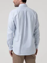Camisa de manga larga de algodón celeste con sutil patrón a cuadros, cuello camisero, cierre frontal con botones y un bolsillo en el pecho con logo bordado.