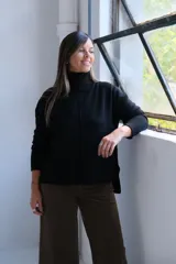Polerón negro de cuello alto, con diseño de costura vertical central y puños acanalados. Presenta un corte holgado con dobladillo asimétrico, siendo más largo en la parte posterior.