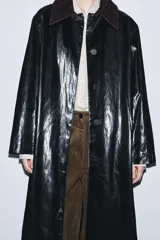 Trench de largo midi con acabado brillante efecto vinilo, manga larga y cuello de solapa en tejido de gamuza a contraste. Presenta cierre frontal con botones ocultos y bolsillos laterales integrados en la costura.