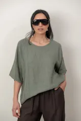 Blusa de lino color marrón oscuro, con escote redondo, mangas cortas amplias y detalle de alforzas verticales en el lateral derecho.