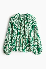 Blusa de manga larga con estampado botánico en verde esmeralda y blanco. Presenta cuello corto fruncido con tapeta de botones y mangas globo con puños finos abotonados.